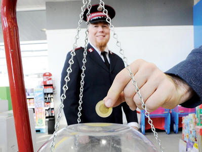 A hand puts a loonie in a Salvation Army kettle.